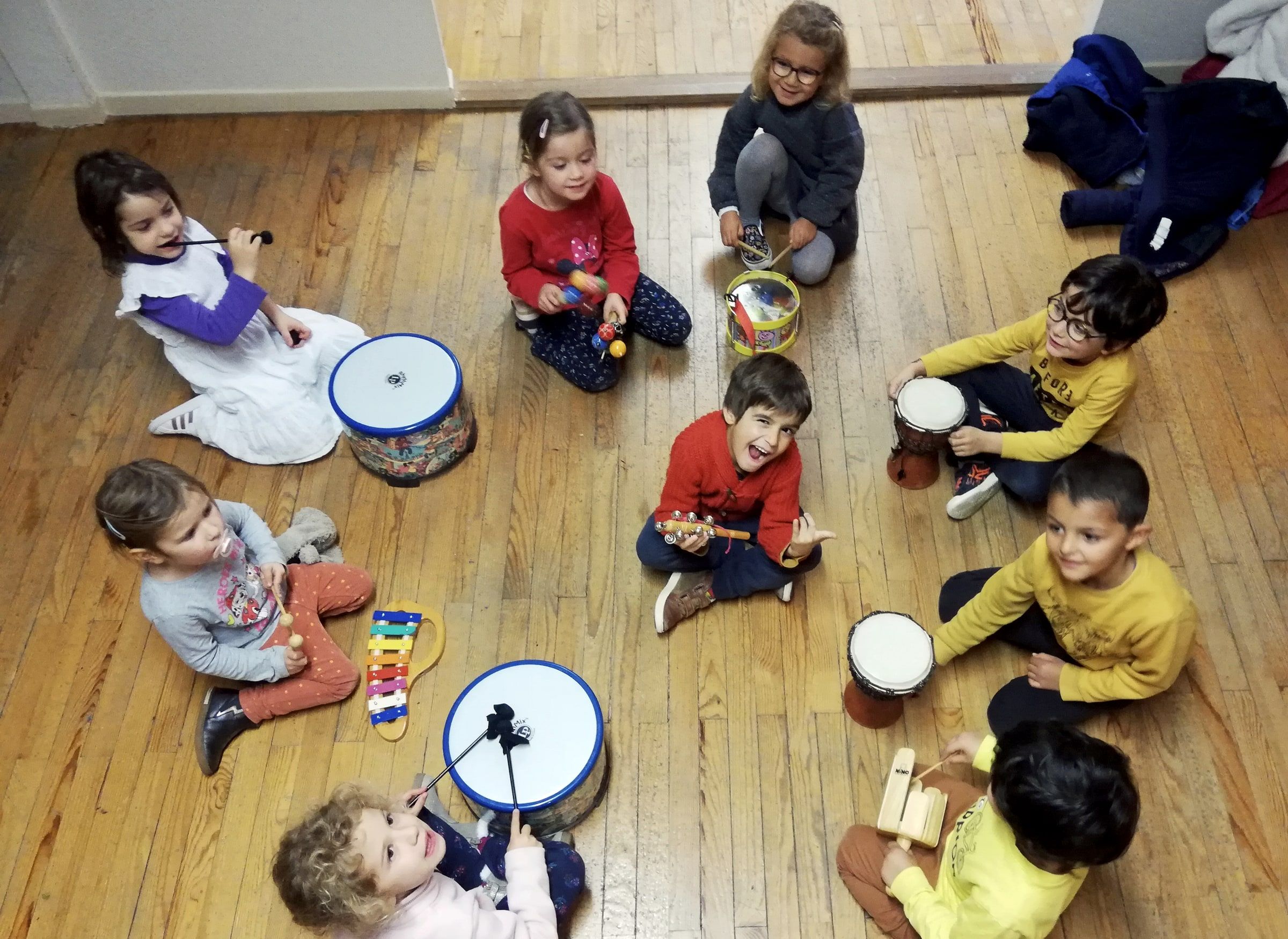 Vue de dessus : les enfants assis en cercle sur le parquet avec tambours et instruments